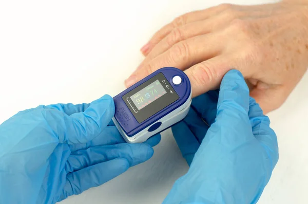 Measurement of saturation in a 60-year-old woman. Doctor\'s hands in medical gloves apply a pulse oximeter to the finger of an elderly woman. Caring for the health of the elderly
