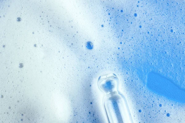 White foam and pipette on a blue background. Macro photo of white shampoo foam or washing foam on a blue background