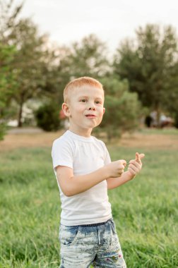 A five-year-old red-haired boy has fun and makes faces in the park on the lawn