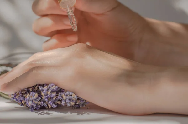 Lavender oil dripping from a pipette on hands, close-up. Female hands hold a pipette with lavender oil