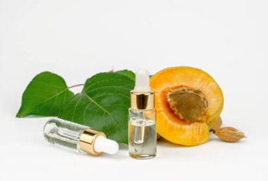 Transparent bottle with apricot essential oil and fresh apricot fruit. Essential oil of apricot and apricot kernels