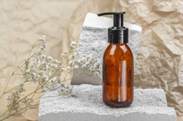 Brown cosmetic bottle with a pump on a white natural stone podium. Body care
