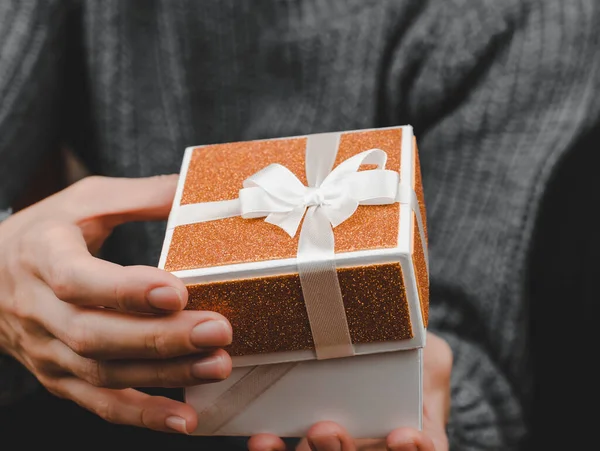 Open gift box in female hands, close-up. Woman opens small golden gift box