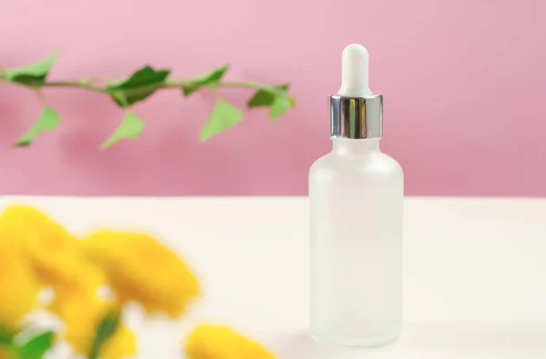 White cosmetic bottle and flowers. Bottle of cosmetic serum or essential oil. Minimal background layout