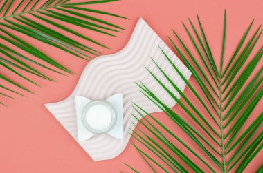 Açık krema kavanozunun üst görüntüsü ve renkli arka planda yeşil yapraklar. Yüz için makyaj ürünleri.