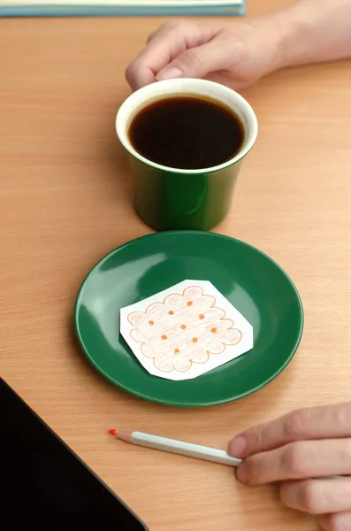 A cup of coffee in hand and a cookie drawn on a piece of paper on a saucer. Concept of economic crisis. Decrease in income. Lowering the standard of living.