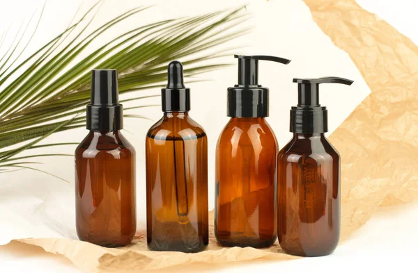 Transparent brown bottles with cosmetics against the background of crumpled parchment paper and palm leaf. Skin and hair care. Selection of cosmetics.