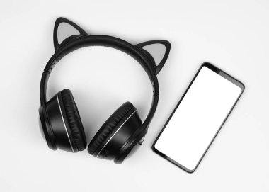 Beyaz arka planda kablosuz kulaklık ve akıllı telefon.