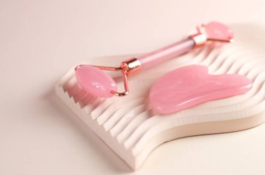 Gül kuvars guaj masajı kazıyıcısı ve sıva geometrik bir podyumda yüz masajı silindiri. Yaşlanma karşıtı tedaviler. Yüz bakımı