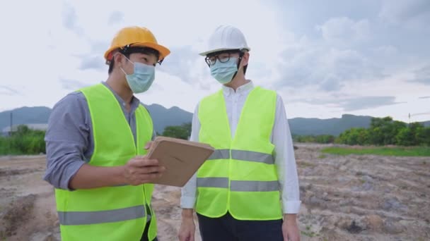 在室外建筑工地大流行期间 亚洲建筑工人戴着医疗面罩 身穿全套安全制服 手持石碑 向经理报告 开展环境友好型项目 — 图库视频影像