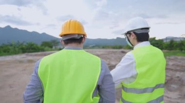 İki Asyalı işçi inşaat alanında çalışma, kontrol ve araştırma sürecini tartışıyor, ustabaşının tavsiyelerini ve fikirlerini uyduruyor, taşınabilir dijital tableti tutuyor, projedeki teknolojiyi kullanıyor, çeşitli uzmanlar bir proje üzerinde birlikte çalışıyorlar.