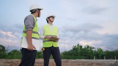 İnşaat alanındaki plan detaylarını tartışan kablosuz cihazlar kullanan çeşitli uzmanlar, inşaat mühendisi, mimari, takım çalışması konsepti olan boş arazi inşaatı, çeşitli uzmanlar proje üzerinde birlikte çalışıyorlar.