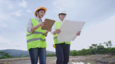 Asyalı mühendis inşaat işçileri proje üzerinde tasarım yapısını tartışıyor ve yürüyorlar, tablet, takım çalışması beyin fırtınası işbirliği, doğal gün ışığı, proje üzerinde birlikte çalışan çeşitli uzmanlarla küçük detaylarla kontrol ediyorlar.