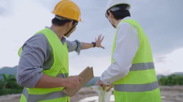 亚洲建筑工人和工程师身穿安全背心 头戴安全帽 在建筑工地一起工作 拿着石板设计图纸 看着现场工作 团队精神讨论规划 各种专家在项目上一起工作 — 图库视频影像