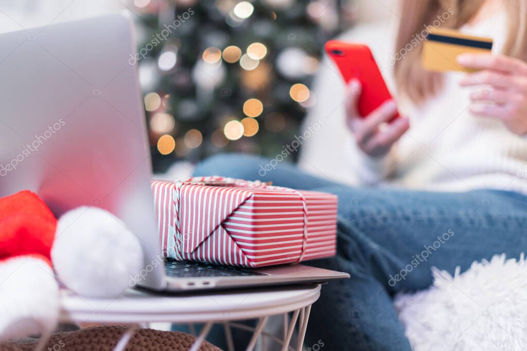 Close up of woman with mobile phone, credit card, present gift box and laptop. Online shopping at Christmas holidays. Freelance girl woking from home office. Merry Christmas and happy new year