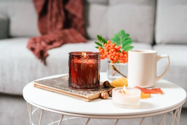 Still life book, candle, rowan berry and a cup of tea or coffee in the living room on a table, home decor in a cozy house. Autumn weekend concept, blanket and plaid. Fallen leaves and home decoration. — Stock Photo, Image