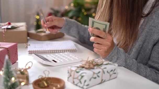 Kız Amerikan dolarlarını sayıyor, hesap makinesi kullanıyor ve masrafları yazıyor. Bütçeyle uğraşan bir kadın, alışveriş çılgınlığı için para dengesini hesaplıyor. Vergi ödeyen kadın muhasebeci. Kız Noel hediyelerini sayıyor — Stok video