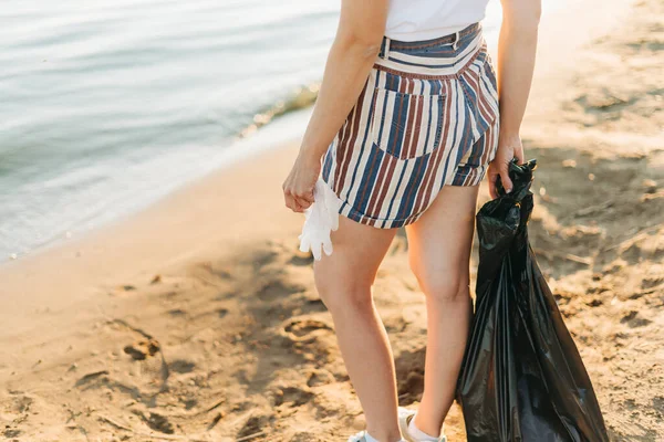 Beschnittene Freiwillige mit Tasche und Handschuhen sammeln Müll, Plastikflaschen, säubern den Strand mit dem Meer. Frau beim Müllsammeln. Umweltökologisches Verschmutzungskonzept. Tag der Erde — Stockfoto