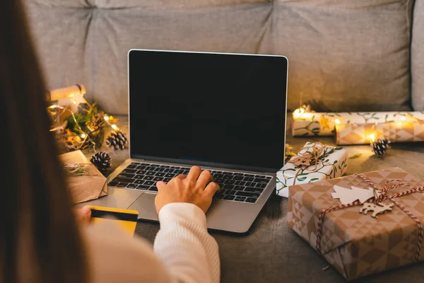 Κοντινό πλάνο των γυναικών χέρια με πιστωτική κάρτα, δώρα, και mock up οθόνη laptop. Online αγορές στις διακοπές των Χριστουγέννων. Καλλιεργημένη γυναίκα κάθεται στον καναπέ με φυσικά οικολογικά δώρα και διακόσμηση. Καλά Χριστούγεννα. — Φωτογραφία Αρχείου