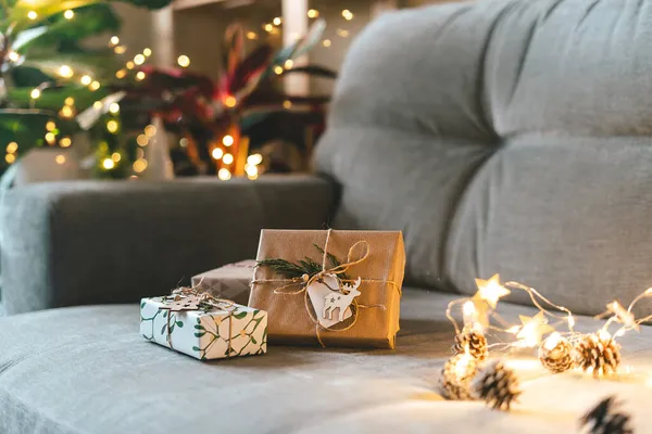 Vánoce přírodní eko dárkové krabice s prázdným štítkem na šedém gauči pozadí v útulném domě. Žhnoucí bokeh, jehličnatá větev. Zimní prázdniny. Bez odpadu, bez plastu. Vnitřní závody. — Stock fotografie
