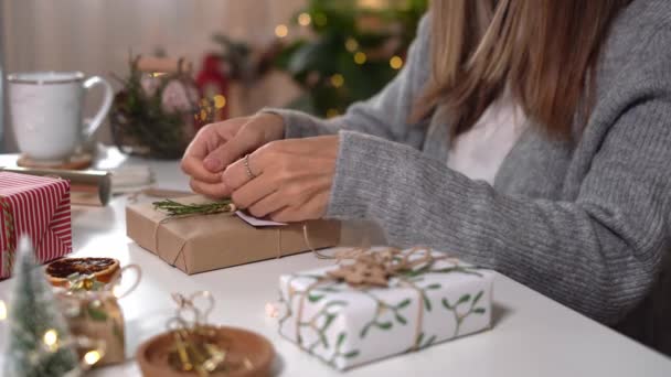 Női kezek csomagolása karácsonyi ajándékdobozok, közelről. Felkészületlen ajándékok fehér asztalon díszítő elemekkel és tárgyakkal Karácsonyi vagy újévi barkácsolás koncepció — Stock videók