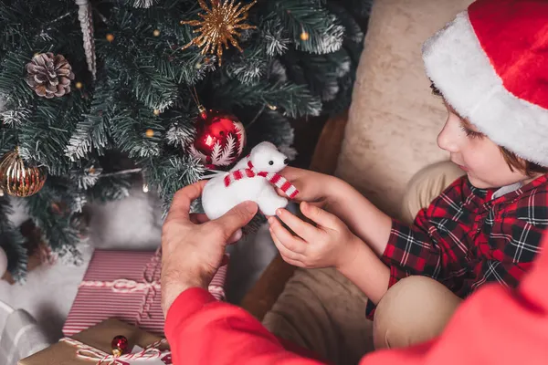 Primer plano de niño y padre manos colgando juguete decorativo en la rama del árbol de Navidad — Foto de Stock
