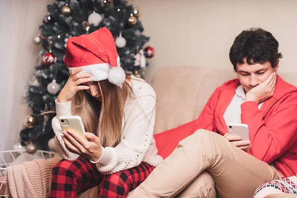 Portret smutnej pary męża i żony z laptopem w czerwonym kapeluszu Mikołaja o wideo rozmowy z pieskiem w swetrze, Boże Narodzenie w domu. Wiadomości online. — Zdjęcie stockowe
