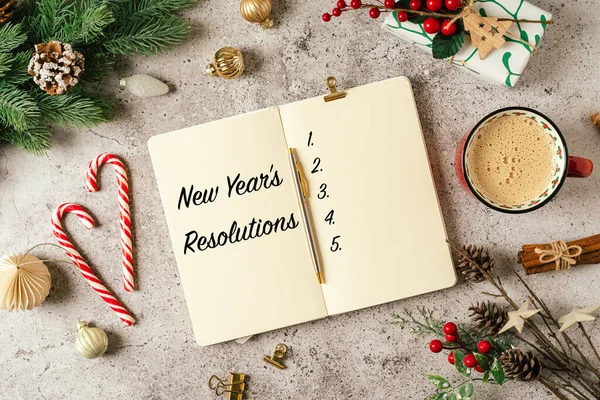 New year resolution text with blank notepad, writing goals . Flat lay of gray background with mug of coffee and Christmas decoration. Top view mock up and copy space for text
