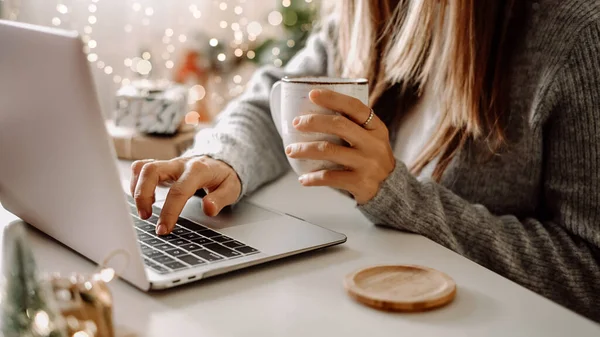 Kadın eli, hediyeler, kahve fincanı ve dizüstü bilgisayar yakın çekim. Noel tatilinde online alışveriş. Ev ofisinden serbest çalışan bir kız. Defter bilgisayarında daktilo eden bir kadın. Noel anları — Stok fotoğraf