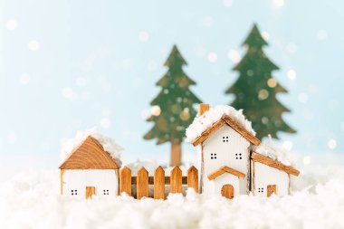 Mutlu yıllar ve mutlu Noeller kartpostalları. Oyuncak ahşap evle, karla, aydınlık bokeh 'le, noel ağacıyla, köyle ve dekorasyonla şenlikli mavi bir arka plan. Kış tatili tebrik kartı için boşluk kopyala