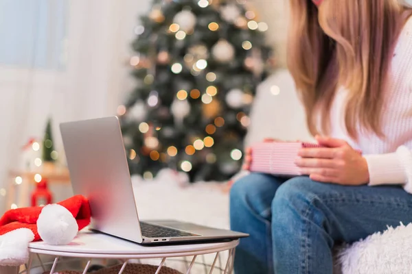 Rozkojarzona kobieta zapakowała świąteczne pudełko z laptopem w domu. Zakupy online w święta Bożego Narodzenia. Choinka, Santa kapelusz i wystrój — Zdjęcie stockowe