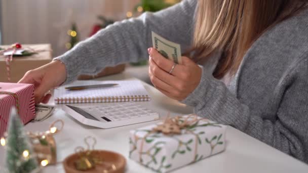 Chica contando billetes de dólar, usando calculadora, y gastos de escritura. Mujer haciendo presupuesto, estimando saldo de dinero para ir de compras. La contadora paga impuestos. Chica contando regalos de Navidad — Vídeos de Stock