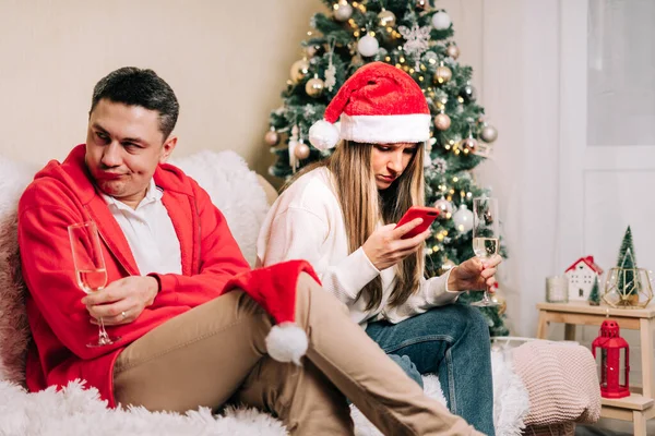 Portrait de couple déprimé homme et femme utilisant un téléphone portable pendant la fête de Noël. Femme fatiguée et mari passer un moment stressant tout en utilisant le téléphone mobile. dispute familiale après la célébration du nouvel an — Photo