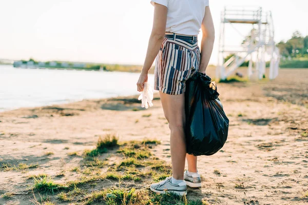 Beschnittene Freiwillige mit Tasche und Handschuhen sammeln Müll, Plastikflaschen, säubern den Strand mit dem Meer. Frau beim Müllsammeln. Umweltökologisches Verschmutzungskonzept. Tag der Erde — Stockfoto