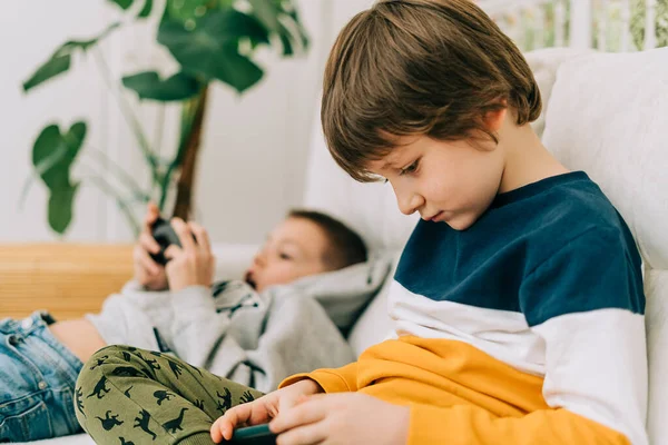 Glada två Childs pojkar spelar online-spel, titta på video på mobilen. Leende barn som använder roliga mobilappar, njuter av gratis fritid hemma på soffan. Bröder leker tillsammans i telefon — Stockfoto