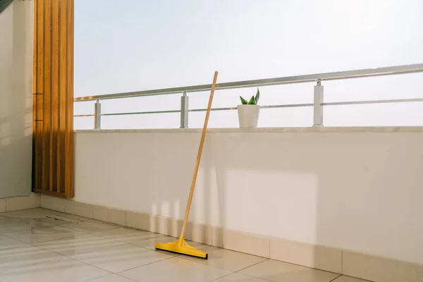 Broom standing on the balcony tiled floor in the summer day. Cleaning equipment with flower pot on the balcony railings. Summer sunny day in the patio — Stok fotoğraf