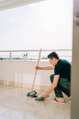 Adam paspasla yerleri siliyor. Temizlikçi kirli yerleri yıkıyor. Güneşli bir günde balkon paspaslayan bir adam. Ev işleri yapan biri. Genç adam yüzeyi temizlemek için temizlik malzemesi kullanıyor.
