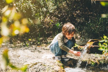 Okullu çocuk dağ deresinden su içiyor. Turist çocuk günlük giysiler içinde yürürken avuçlarından bir yudum nehir suyu içiyor.