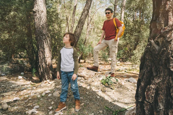 Szkolny turysta i jego ojciec spacerują po wiosennym lesie. Chłopiec i ojciec ubrani w luźne ubrania wędrujący latem po zielonym lesie liściastym. Rodzinna przygoda w lesie — Zdjęcie stockowe