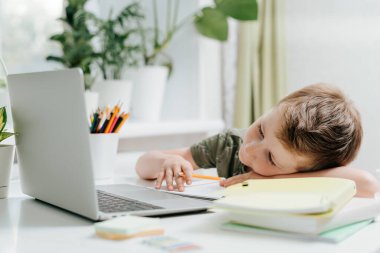 Çocuk laptopta ders çalışıyor, uyumaktan ve not defterinde uyumaktan yoruluyor, okul ödevi yapıyor. Kafkas Çocuk elinde defter ve eğitim kitabıyla oturuyor. Okula dönelim. Uzaklık öğrenimi çevrimiçi eğitim.