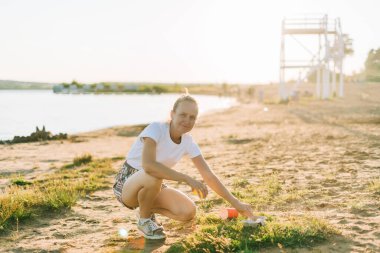 Genç bayan gönüllü çöpleri, plastik şişeleri ve kahve fincanlarını toplamaktan, sahili denizle temizlemekten memnun. Çöp toplayan kadın. Çevresel ekoloji kirliliği kavramı. Dünya Günü.
