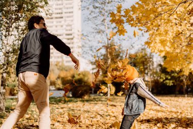 Father and son having fun in autumn park with fallen leaves, throwing up leaf. Child kid boy and his dad outdoors playing with maple leaves