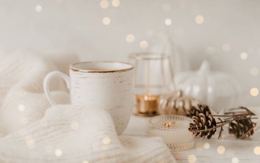 Sakin hayat, bir fincan çay ya da kahve, balkabağı, mum, beyaz masa arkasında yapraklı brunch, rahat bir evde ev dekorasyonu. Sonbahar hafta sonu konsepti. Düşmüş yapraklar ve ev dekorasyonu