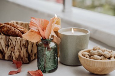 Durgun mum alevi, yer fıstığı, düşen yapraklar, hasır sepet, masada simit, rahat bir evde ev dekorasyonu. Sonbahar hafta sonu konsepti 
