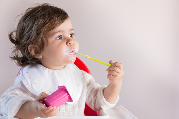 Baby girl eating yogurt with messy face
