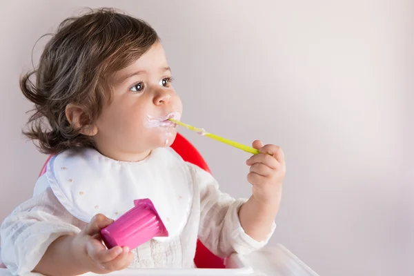 乱雑な顔とヨーグルトを食べる女の赤ちゃん ロイヤリティフリーのストック画像