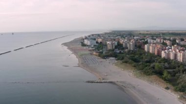 Şemsiyeli, çarşaflı ve kasabalı kumlu sahil manzarası. Lido Adriano kasabası, Adriyatik kıyısı, Emilia Romagna, İtalya.