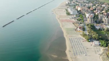 Şemsiyeli, çarşaflı ve kasabalı kumlu sahil manzarası. Lido Adriano kasabası, Adriyatik kıyısı, Emilia Romagna, İtalya.