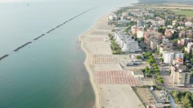 Şemsiyeli, çarşaflı ve kasabalı kumlu sahil manzarası. Lido Adriano kasabası, Adriyatik kıyısı, Emilia Romagna, İtalya.