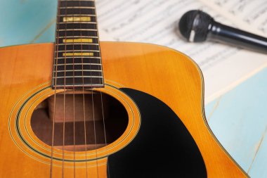 Gitar, müzik kağıtları ve siyah mikrofonlu müzik kaydı sahnesi ahşap masada, yakın plan.